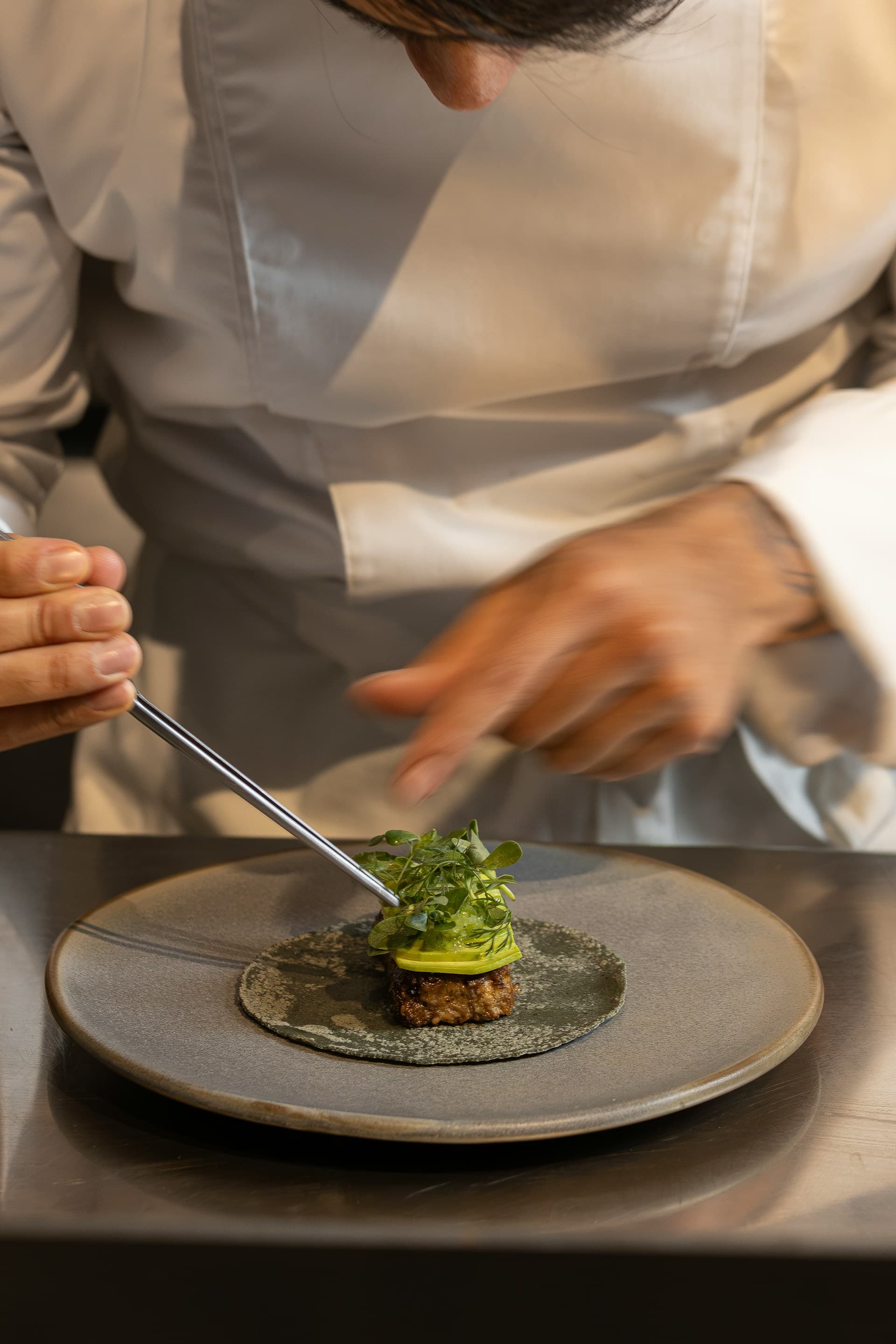 Chef plating a fine dining dish with tweezers and micro herbs — bespoke event catering by House of Nelle